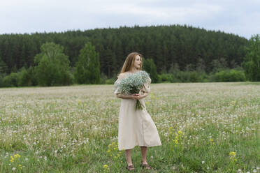 Schöne junge Frau hält Blumenstrauß auf Feld - SEAF01993