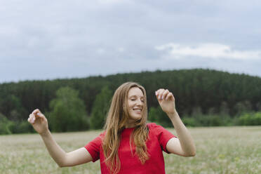 Lächelnde junge Frau in rotem T-Shirt tanzt auf einem Feld - SEAF02006