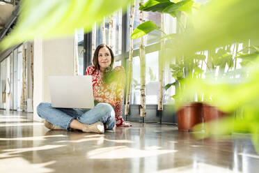 Smiling businesswoman sitting on floor with laptop - PESF03940