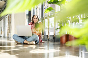 Lächelnde Geschäftsfrau auf dem Boden sitzend mit Laptop - PESF03940