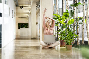 Happy businesswoman stretching arms in corridor - PESF03942