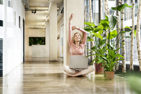 Happy businesswoman stretching arms in corridor - PESF03942