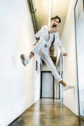 Junger Geschäftsmann benutzt sein Smartphone und springt in den Korridor - PESF03950