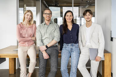 Happy business colleagues leaning on desk in office - PESF03968