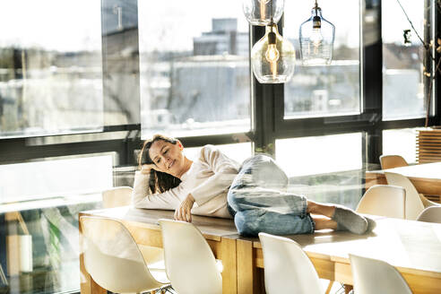 Smiling businesswoman lying on table seen through glass - PESF03971