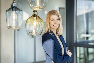 Happy blond businesswoman standing with arms crossed - PESF03974