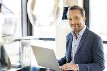 Happy businessman with laptop in office cafeteria - PESF03980