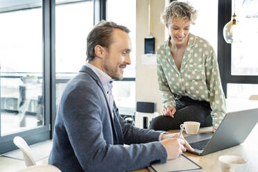 Happy business colleagues discussing together over laptop in office - PESF03984