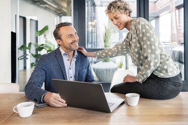 Happy business colleagues discussing over laptop in office cafeteria - PESF03985