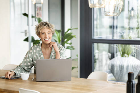 Lächelnde Geschäftsfrau sitzt mit Laptop am Tisch - PESF03995