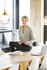 Smiling blond businesswoman sitting with tablet PC - PESF03997