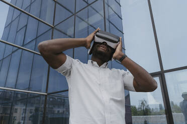 Businessman using virtual reality headset in front of office building - OSF01687