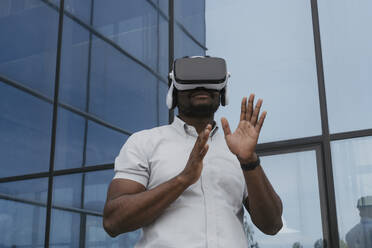 Businessman watching through virtual reality headset in front of office building - OSF01688