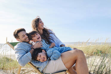 Glückliche Familie umarmt Vater auf Stuhl am Strand - ASGF03758