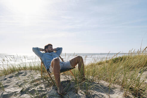 Man relaxing on chair at beach on sunny day - ASGF03759