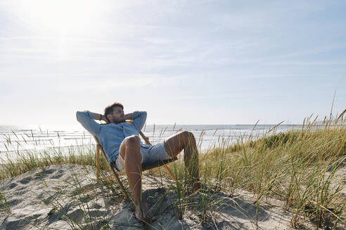 Mann entspannt sich auf einem Stuhl am Strand an einem sonnigen Tag - ASGF03759