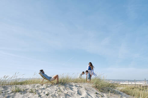 Vater entspannt sich auf einem Stuhl mit seiner Familie und verbringt seine Freizeit am Strand - ASGF03766