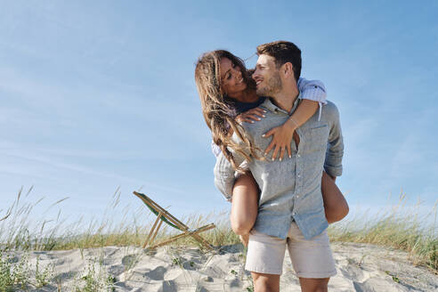 Romantischer Mann nimmt Freundin am Strand huckepack - ASGF03770