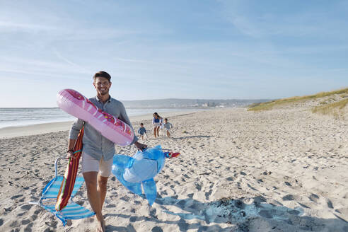 Vater trägt aufblasbare Schwimmringe am Strand an einem sonnigen Tag - ASGF03774