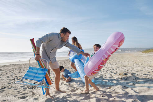 Family with inflatable swim rings enjoying at beach on sunny day - ASGF03776