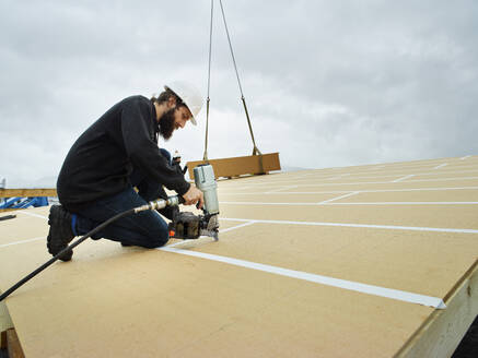 Carpenter using nail tool on wooden rooftop - CVF02423