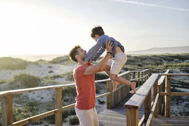 Father carrying son from boardwalk railing at beach - ASGF03779