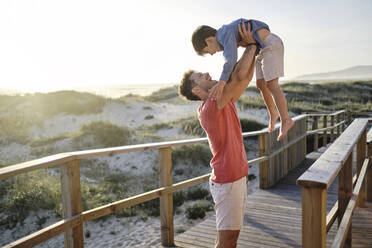 Vater trägt seinen Sohn auf der Promenade am Strand - ASGF03780