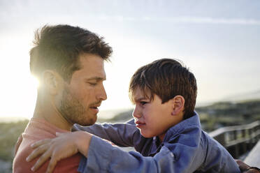 Father comforting crying son at beach - ASGF03785