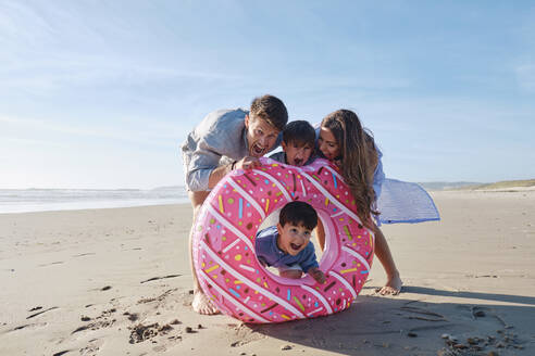 Playful family with doughnut shaped inflatable ring at beach - ASGF03793