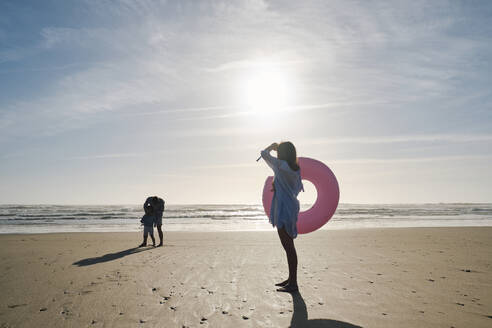 Woman holding inflatable swim ring at beach on sunny day - ASGF03795