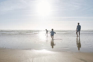 Father playing with children at beach on sunny day - ASGF03797