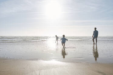 Vater spielt mit Kindern am Strand an einem sonnigen Tag - ASGF03797