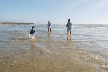 Junge läuft im Meerwasser mit Familie am Strand an einem sonnigen Tag - ASGF03803