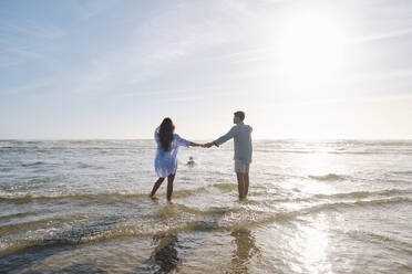 Paar, das sich an den Händen hält, steht im Meer an einem sonnigen Tag - ASGF03805