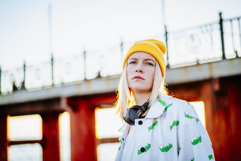 Blond young woman with white outfit standing in front of bridge - MDOF01344