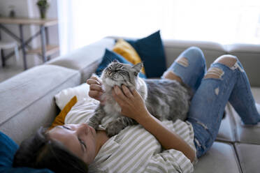 Woman lying on sofa and stroking cat at home - ANNF00330
