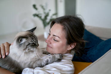 Smiling woman with cat lying on sofa at home - ANNF00331