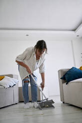 Woman cleaning with broom in living room at home - ANNF00333