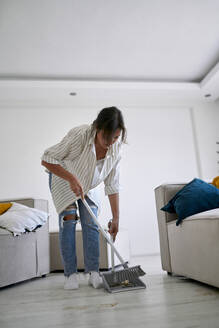 Frau putzt mit Besen im Wohnzimmer zu Hause - ANNF00333