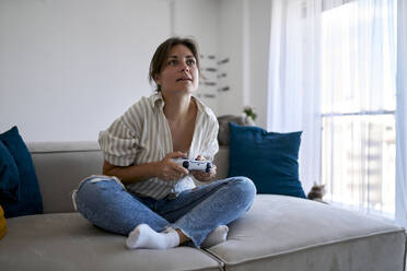 Frau mit Fernbedienung spielt Videospiel zu Hause - ANNF00344