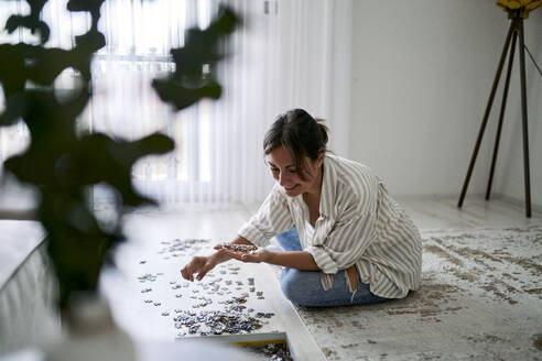 Happy woman playing puzzle in living room at home - ANNF00353