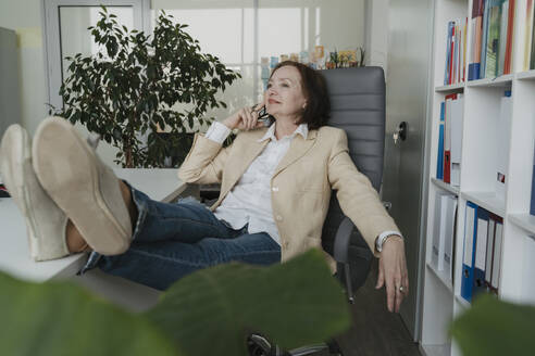 Nachdenkliche ältere Geschäftsfrau entspannt sich auf einem Stuhl im Büro - OSF01702