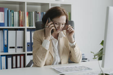 Ältere Geschäftsfrau telefoniert am Tisch sitzend im Büro - OSF01703