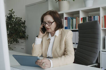 Ältere Geschäftsfrau telefoniert mit einem Tablet-PC am Tisch - OSF01704
