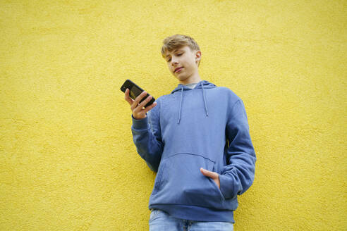 Junge mit Mobiltelefon vor gelber Wand - NJAF00349