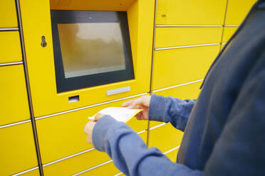 Boy scanning receipt in front of parcel locker - NJAF00355