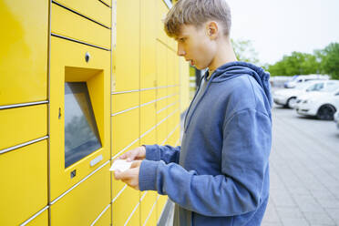 Boy with ticket standing in front of parcel locker - NJAF00357