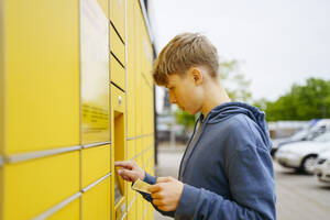 Blonder Junge mit Fahrkarte gibt Daten in einen Paketautomaten ein - NJAF00358