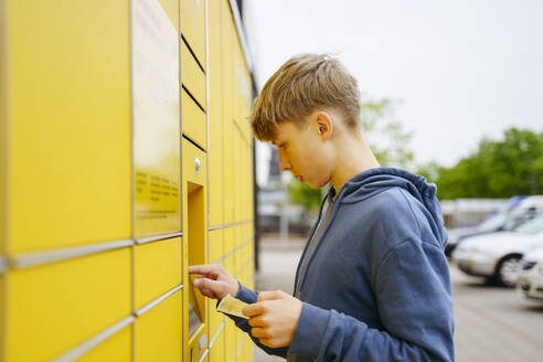 Blonder Junge mit Fahrkarte gibt Daten in einen Paketautomaten ein - NJAF00358