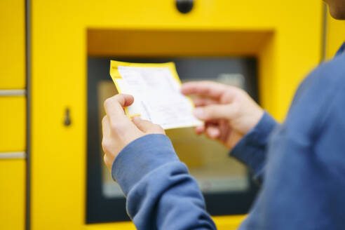 Junge mit Fahrkarte vor einem Paketkasten - NJAF00365